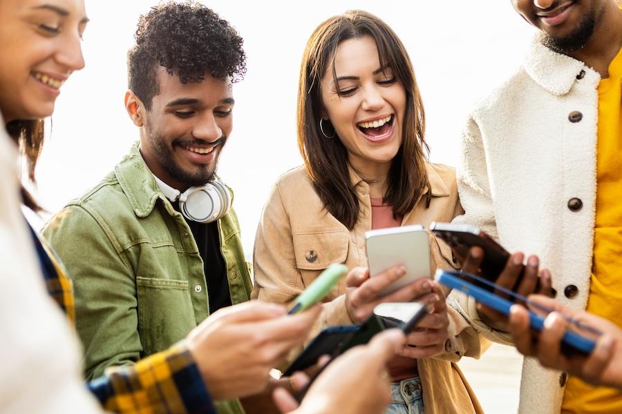 Happy group of four college students using their smartphones outside.